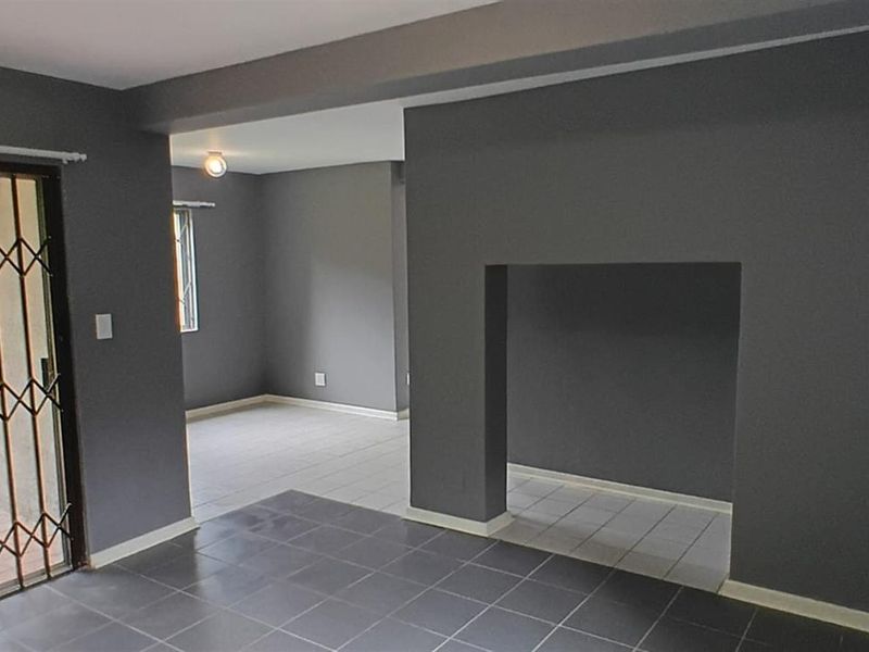 An open-plan living area featuring dark grey walls, tiled flooring, and a sliding glass door with a security gate leading to the exterior.