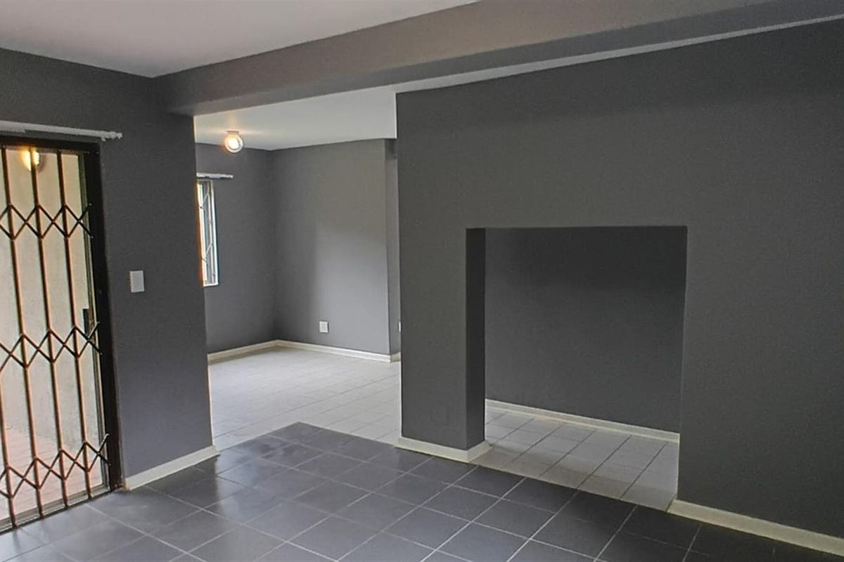 An open-plan living area featuring dark grey walls, tiled flooring, and a sliding glass door with a security gate leading to the exterior.