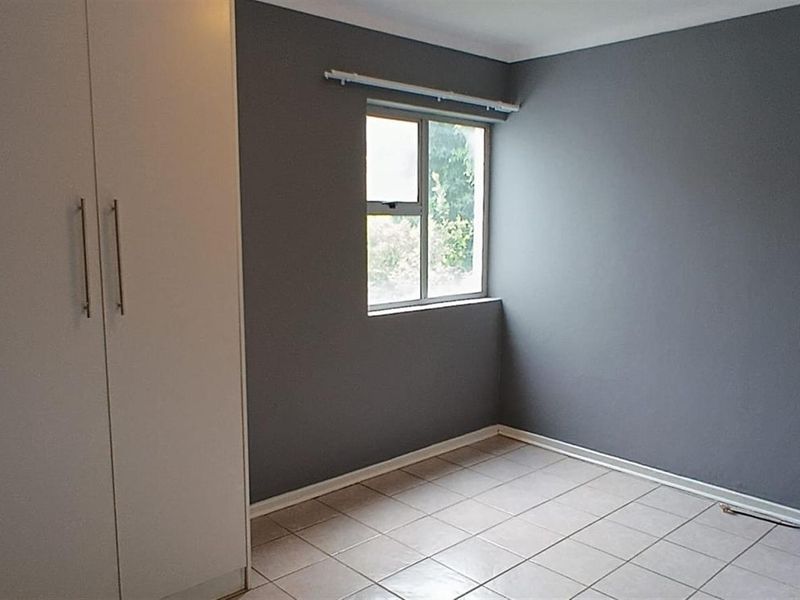 A clean, empty bedroom featuring neutral grey walls, tiled flooring, and built-in cupboards, offering a versatile space ready for personalization.