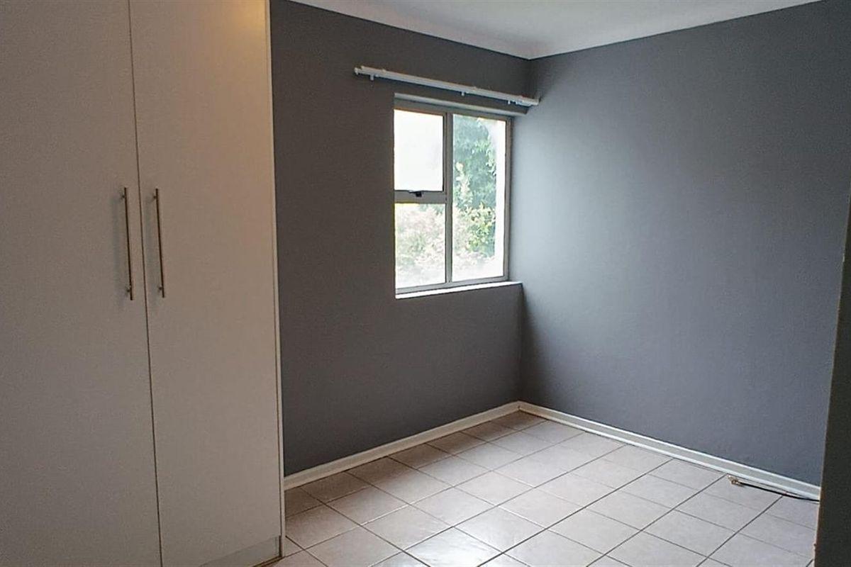 A clean, empty bedroom featuring neutral grey walls, tiled flooring, and built-in cupboards, offering a versatile space ready for personalization.