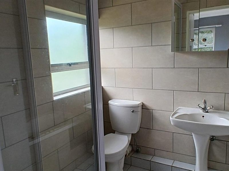 A functional bathroom featuring a shower enclosure, pedestal basin, and toilet with neutral wall tiling.