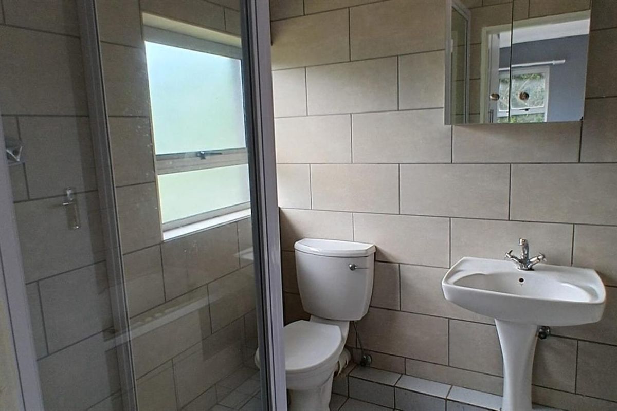 A functional bathroom featuring a shower enclosure, pedestal basin, and toilet with neutral wall tiling.
