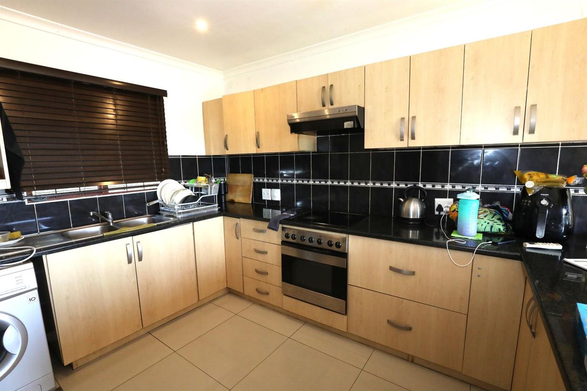 A functional kitchen featuring light wood cabinetry, black granite countertops, black tiled backsplash, and integrated stainless steel oven and extractor fan.