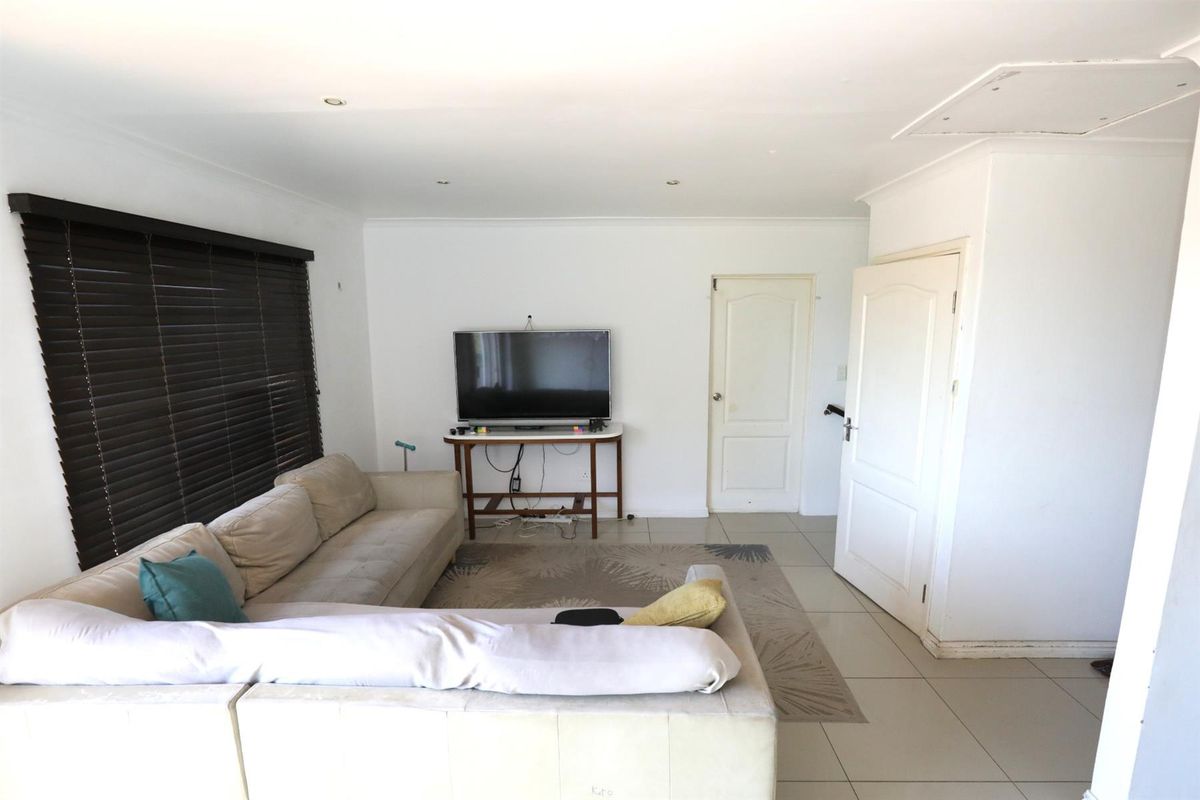 A bright living room featuring tiled flooring, recessed ceiling lighting, and dark window blinds, providing a neutral foundation for interior design.