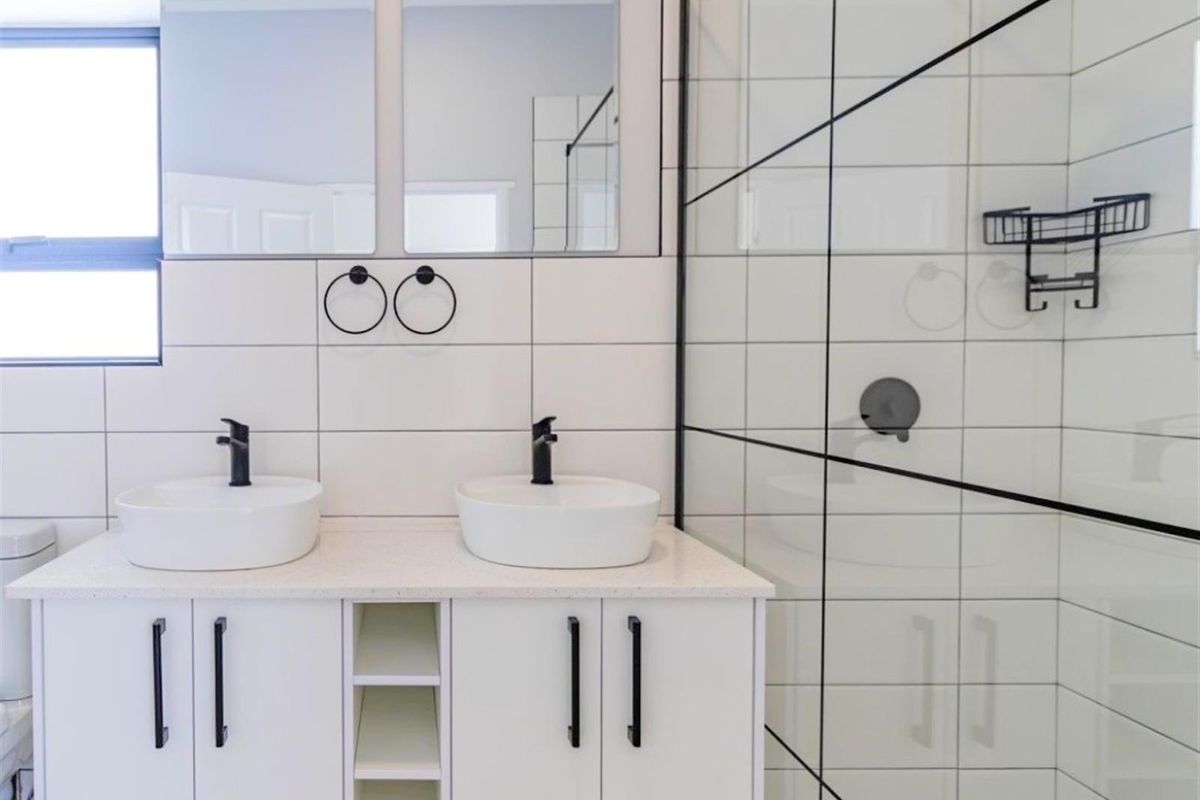 Modern bathroom featuring a double vanity with vessel sinks, matte black fixtures, and a spacious walk-in shower with a glass enclosure.