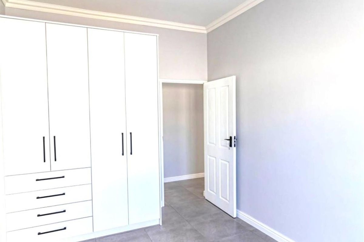 A bright, modern bedroom featuring built-in white cabinetry with sleek black handles, neutral grey floor tiles, and crisp crown molding.