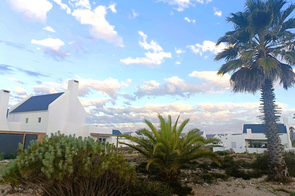 A view of the exterior of the property featuring white facades, dark roofs, and landscaped garden areas with palm trees.