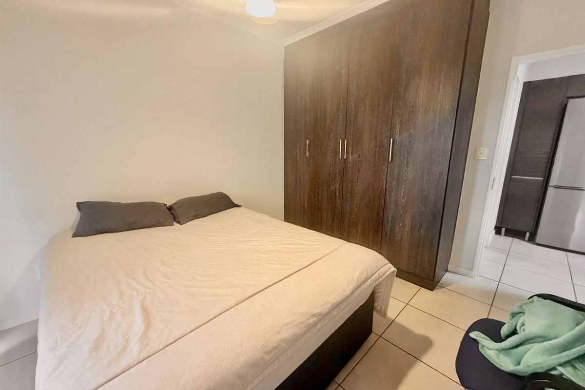 A bedroom featuring tiled flooring and a large, dark wood-finish built-in wardrobe providing ample storage space.