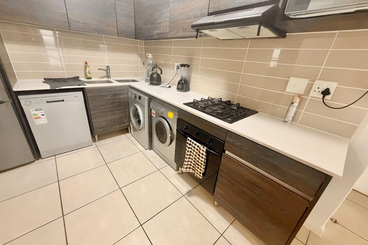 Modern kitchen featuring dark wood cabinetry, stone countertops, gas hob, electric oven, extractor fan, and integrated space for laundry appliances.
