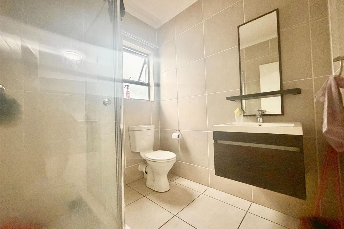 A modern bathroom featuring a glass shower enclosure, wall-mounted vanity with basin, and neutral floor-to-ceiling tiling.