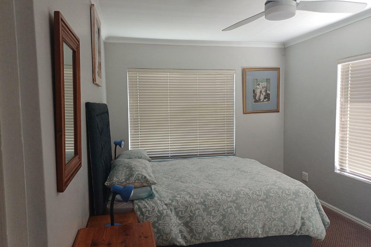 A well-lit bedroom featuring a ceiling fan, neutral wall finishes, and dual windows with fitted blinds, providing a comfortable and functional living space.