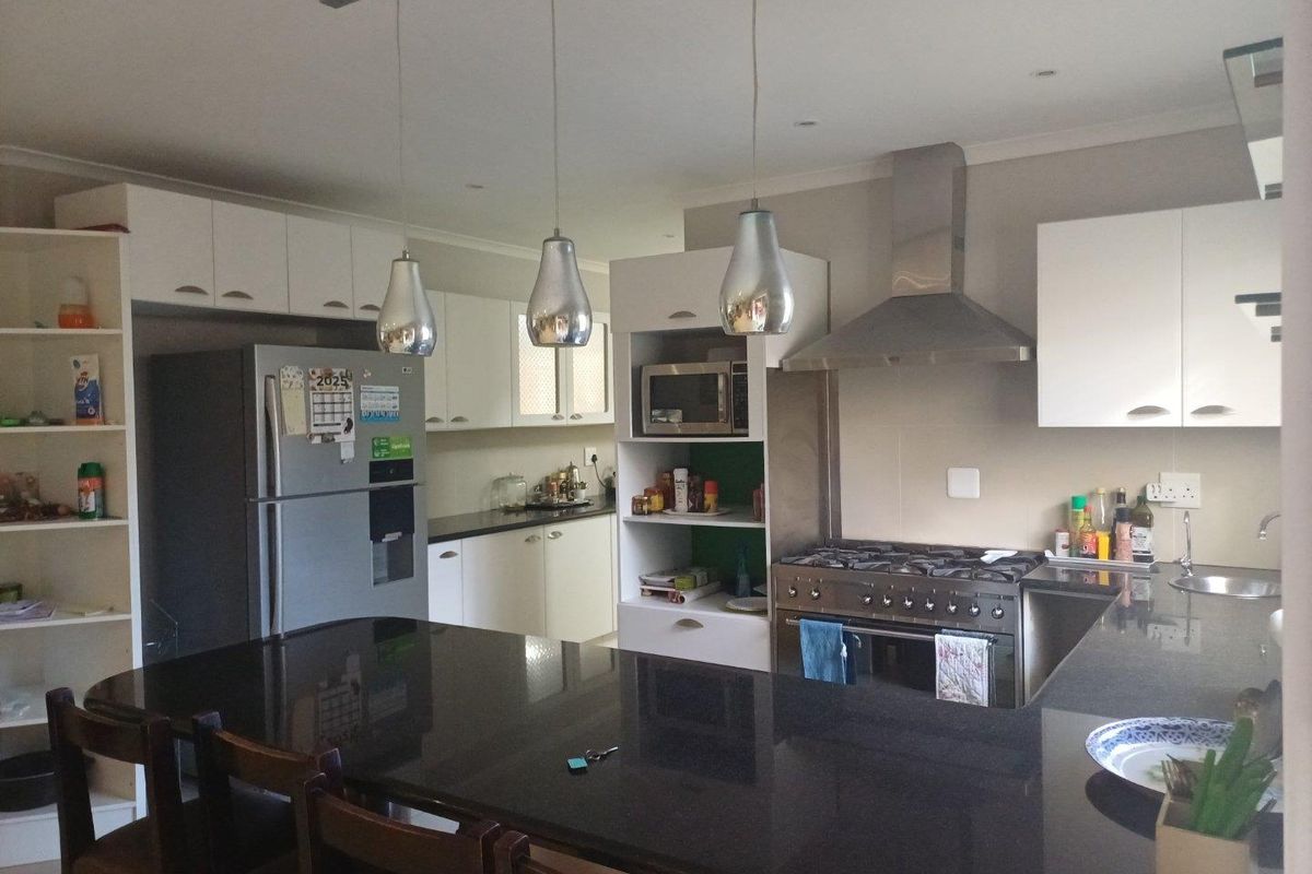 Modern kitchen featuring a large black granite breakfast bar, white cabinetry, stainless steel gas stove, extractor fan, and built-in microwave.