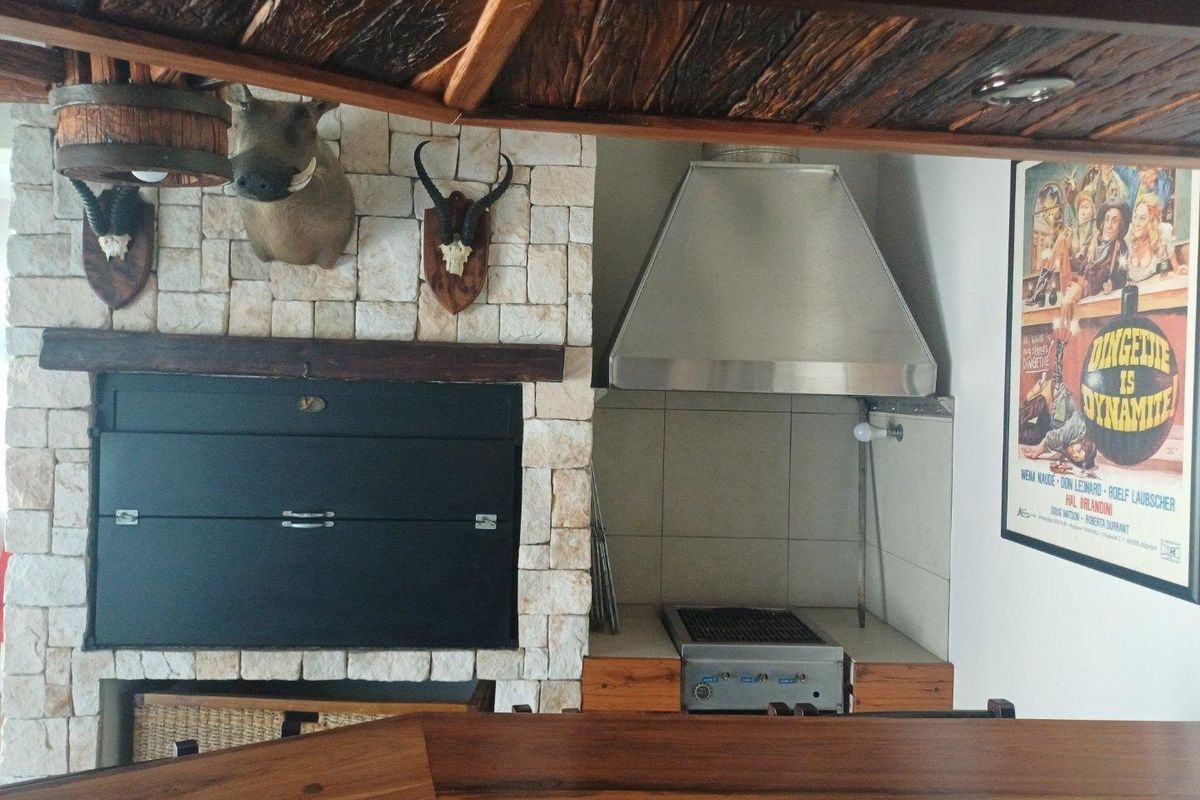 Indoor entertainment area featuring a built-in braai, stone cladding, stainless steel extractor hood, and a wooden bar counter.