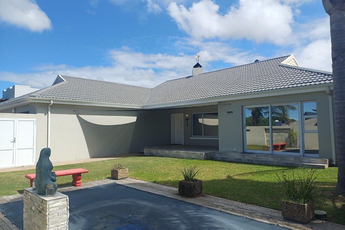 Rear view of the house featuring a tiled roof, sliding glass doors, a covered patio area, and a lawn with a pool cover.