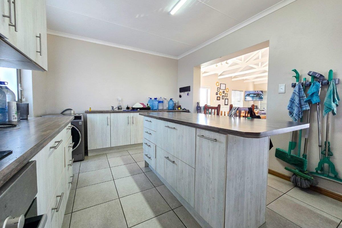 A functional kitchen featuring light wood-grain cabinetry, a central island with a breakfast bar, and tiled flooring, with an open-plan layout to the living area.