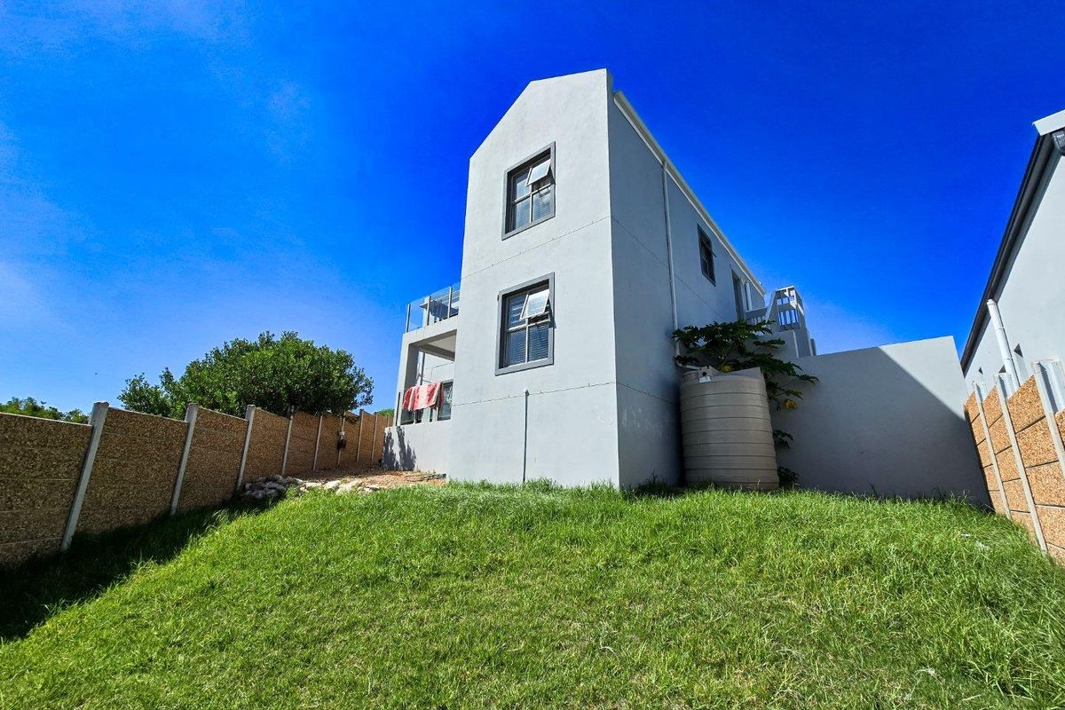Rear view of a two-story house featuring a grass lawn, exterior water tank, and balcony access.