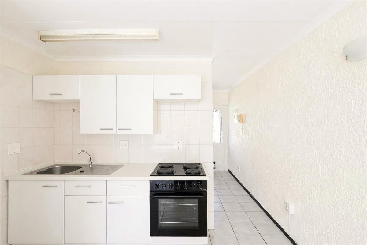 A functional, compact kitchen featuring white cabinetry, a tiled backsplash, and a built-in electric stove and oven, with tiled flooring throughout.