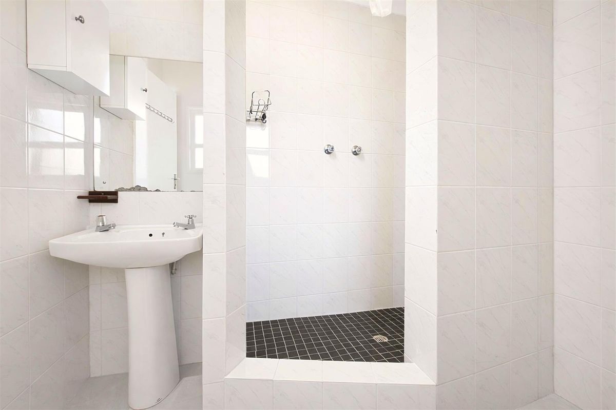 A clean, minimalist bathroom featuring a pedestal sink, wall-mounted cabinetry, and a walk-in shower with contrasting floor tiles.