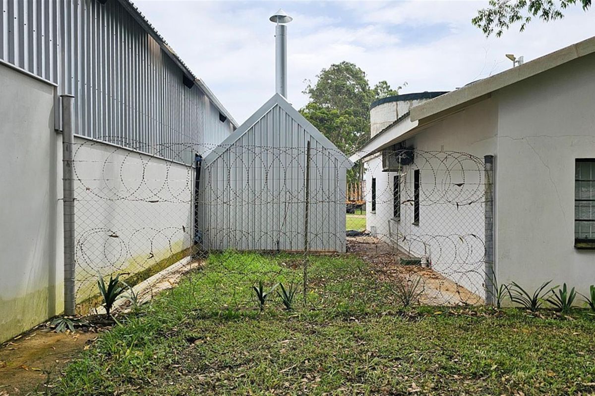 Exterior view of the farm property showing metal outbuildings, security fencing with razor wire, and surrounding grounds.
