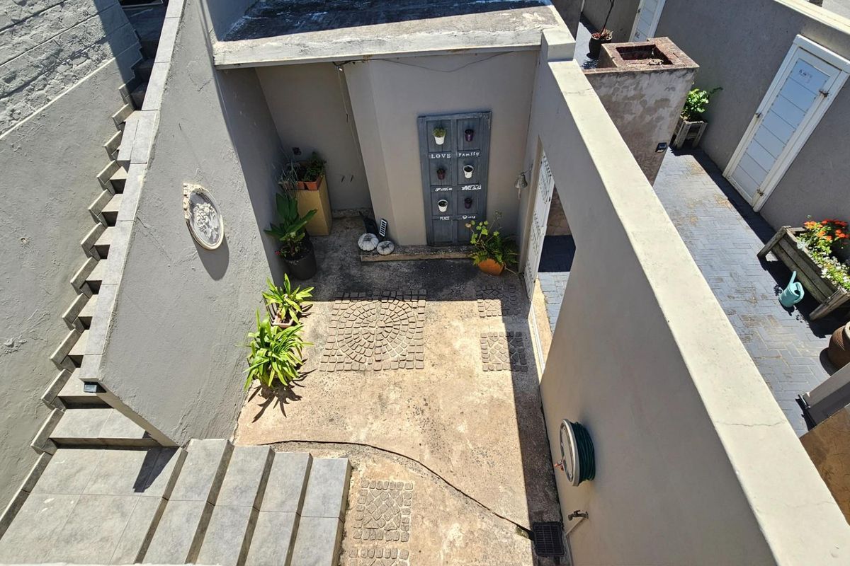An elevated view of a private courtyard featuring concrete stairs, paved flooring, and access to the main dwelling area.