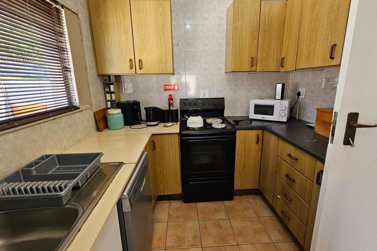 A functional kitchen featuring wood-look cabinetry, tiled splashbacks, a freestanding oven, and a stainless steel sink.