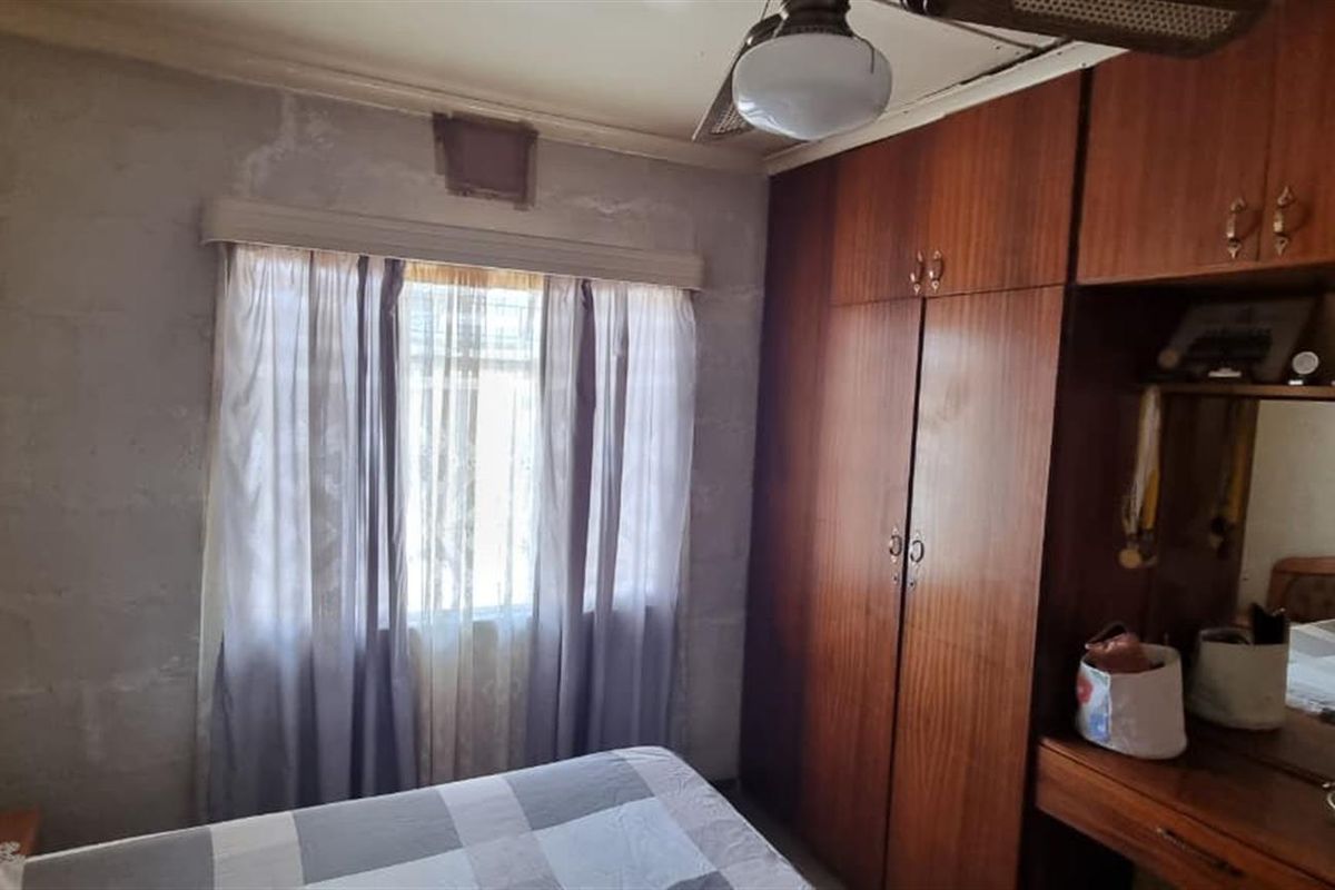 Bedroom featuring built-in wooden cabinetry, a vanity unit, and a ceiling fan, showing signs of wall surface wear and water staining.