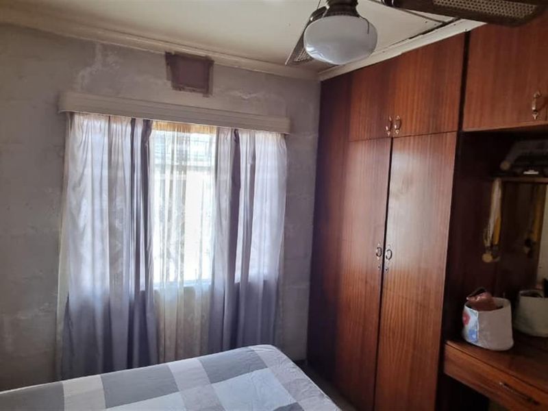 Bedroom featuring built-in wooden cabinetry, a vanity unit, and a ceiling fan, showing signs of wall surface wear and water staining.