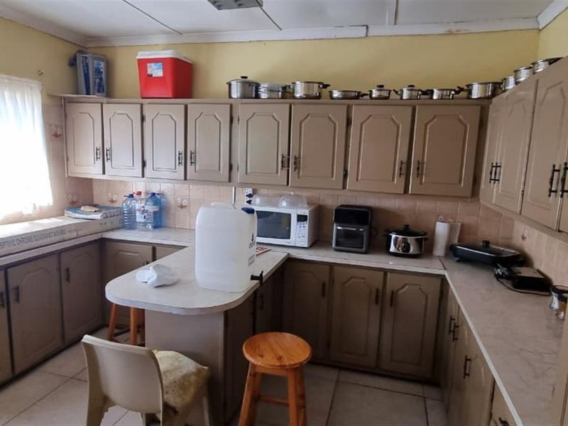 A functional kitchen featuring extensive built-in cabinetry, laminate countertops, and tiled flooring, offering a dated aesthetic with potential for modern renovation.