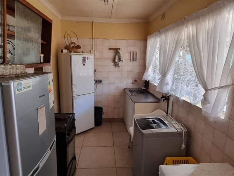 A functional kitchen featuring tiled walls, tiled flooring, and built-in cabinetry with a stainless steel sink, offering potential for modernization.