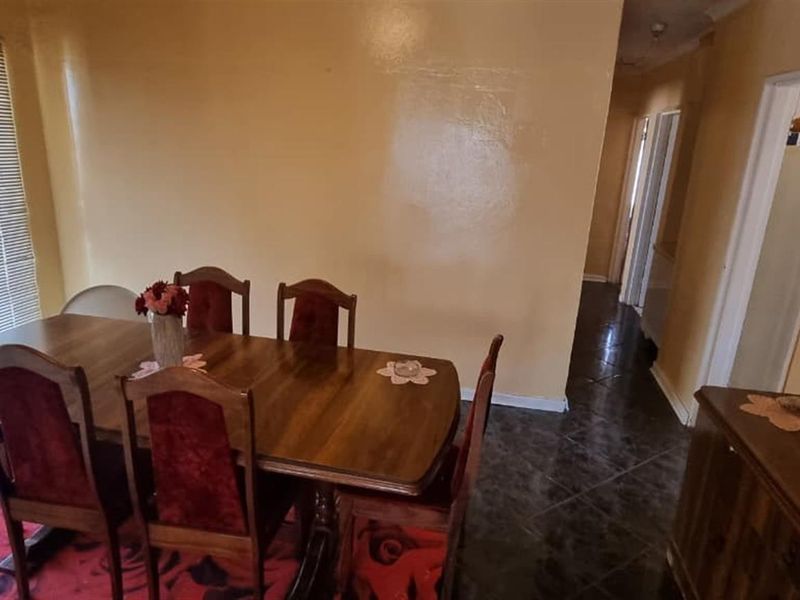 Dining room featuring dark tiled flooring and venetian blinds, providing access to the hallway and adjacent living areas.