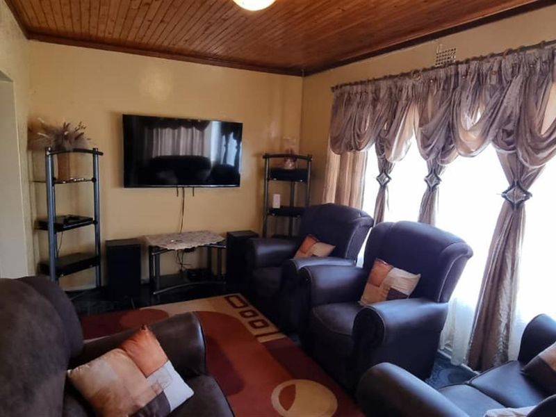 A living room featuring a timber tongue and groove ceiling and large window with curtain rails, offering a dated aesthetic ready for modernization.