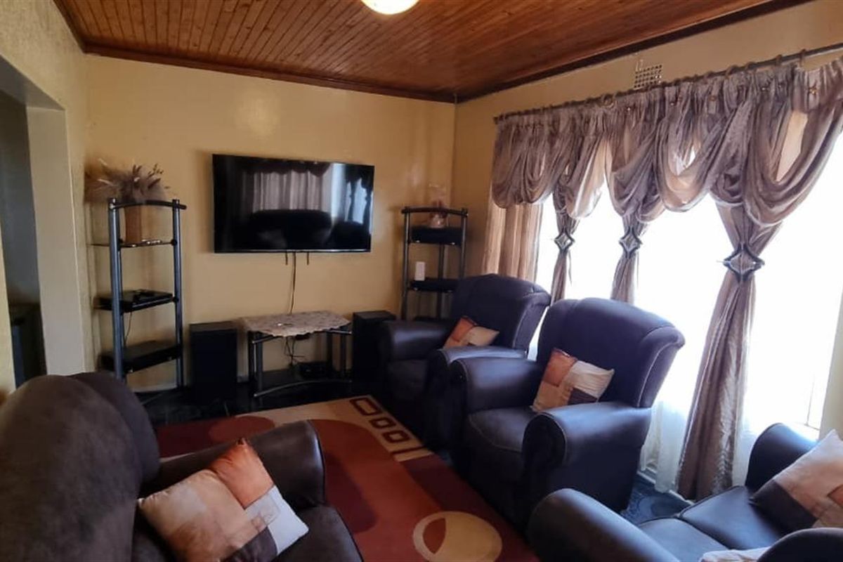A living room featuring a timber tongue and groove ceiling and large window with curtain rails, offering a dated aesthetic ready for modernization.