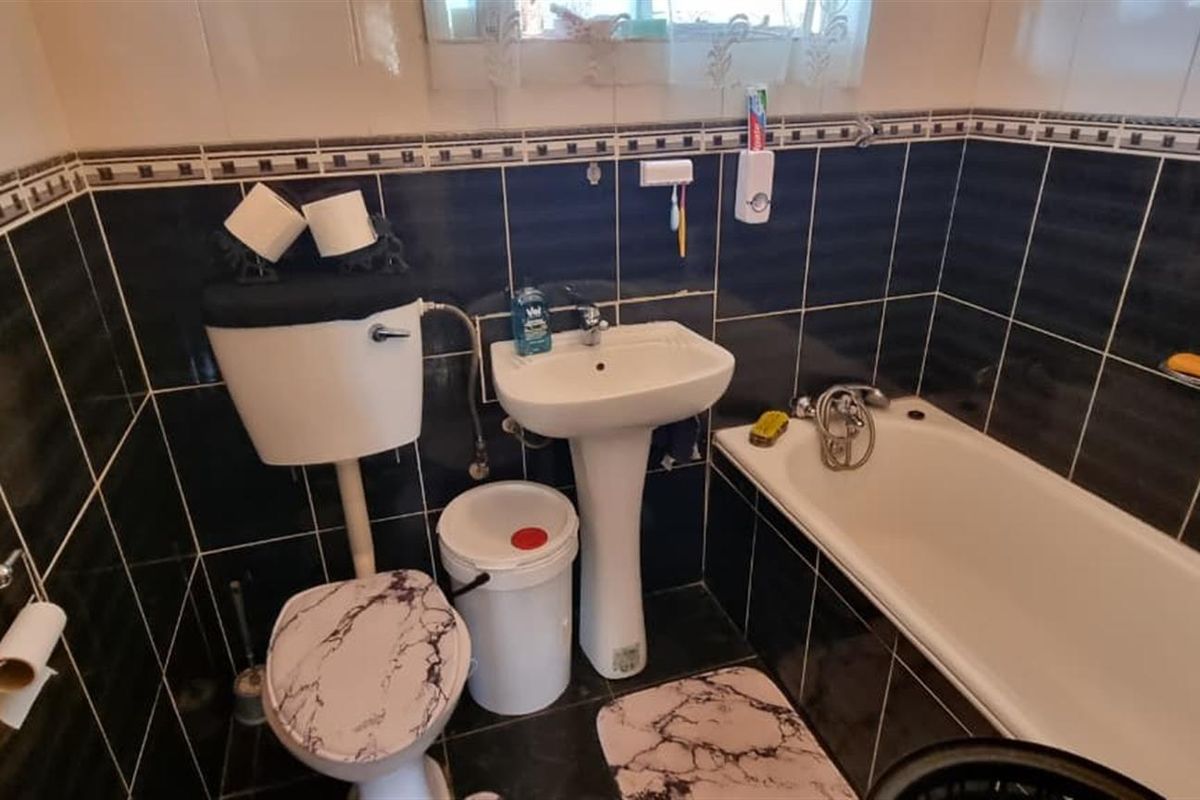 A functional bathroom featuring dark wall tiling, a pedestal washbasin, a close-coupled toilet, and a standard bathtub.