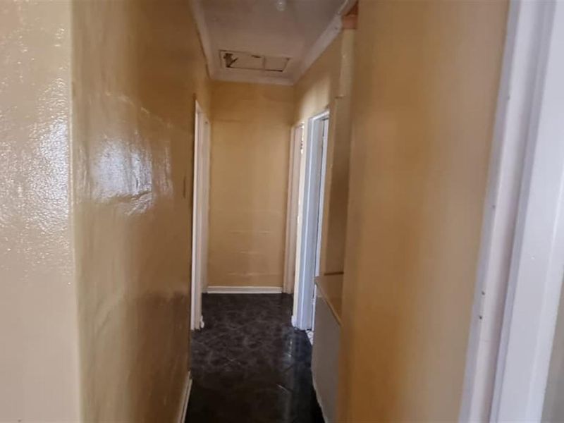 A functional hallway connecting interior spaces, featuring tiled flooring and a ceiling access hatch, requiring cosmetic updates to improve the overall aesthetic.