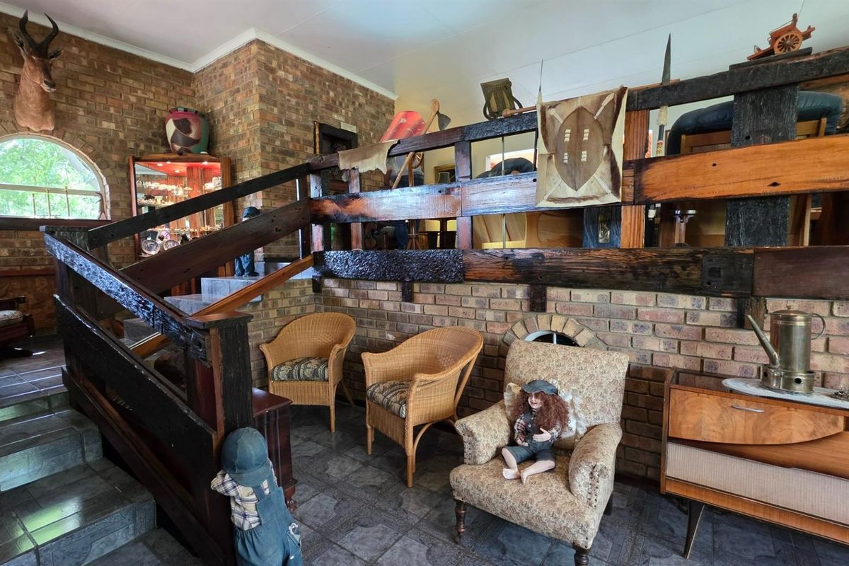 A rustic living area featuring exposed face-brick walls, a prominent timber staircase with a heavy wooden balustrade, and tiled flooring.