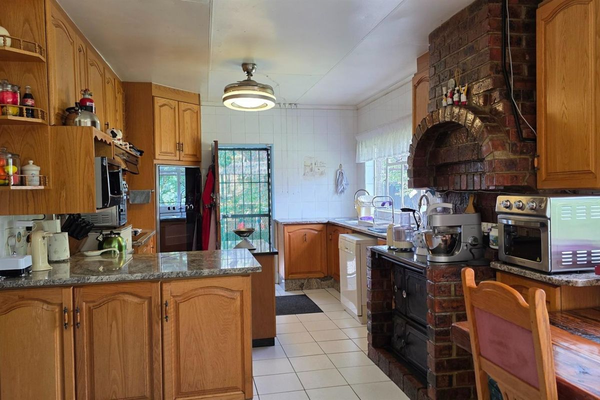 A traditional farm-style kitchen featuring wooden cabinetry, granite countertops, a prominent brick fireplace surround, and tiled flooring.