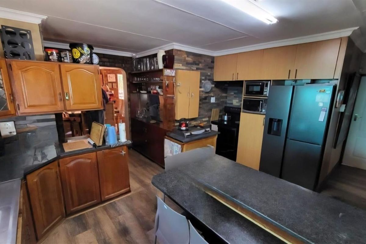 A functional kitchen featuring wood-tone cabinetry, dark laminate countertops, a brick feature wall, and integrated appliances, offering potential for a modern cosmetic update.