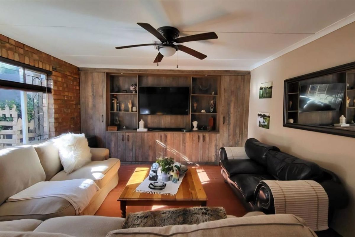 A cozy living room featuring an exposed brick wall, built-in wooden cabinetry, and a ceiling fan, providing a warm and functional living space.