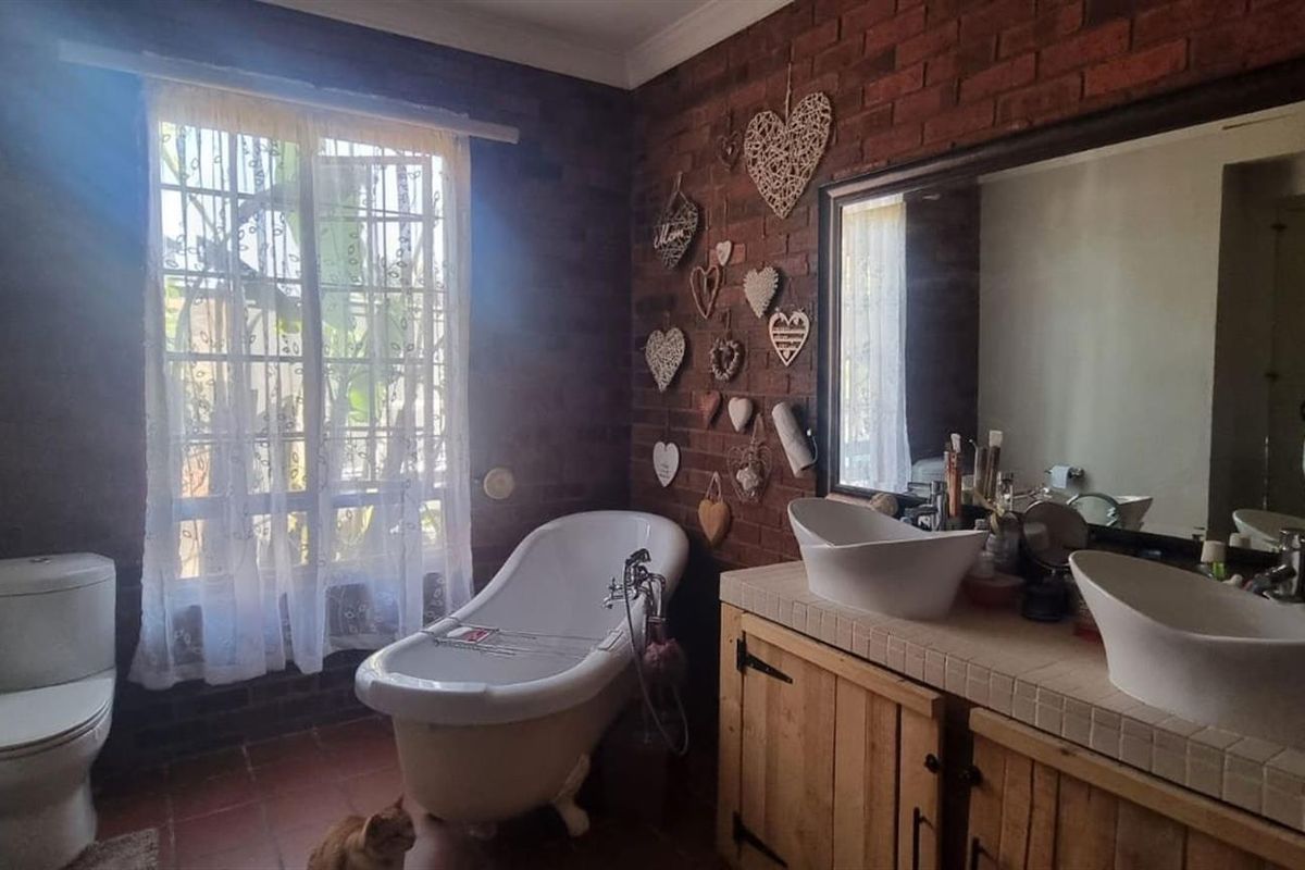 A bathroom featuring an exposed brick wall, a freestanding bathtub, and a dual-sink vanity with a tiled countertop.