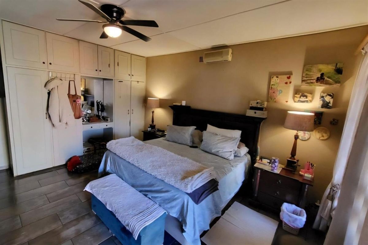 Spacious bedroom featuring built-in cupboards, tiled flooring, a ceiling fan, and a wall-mounted air conditioning unit.