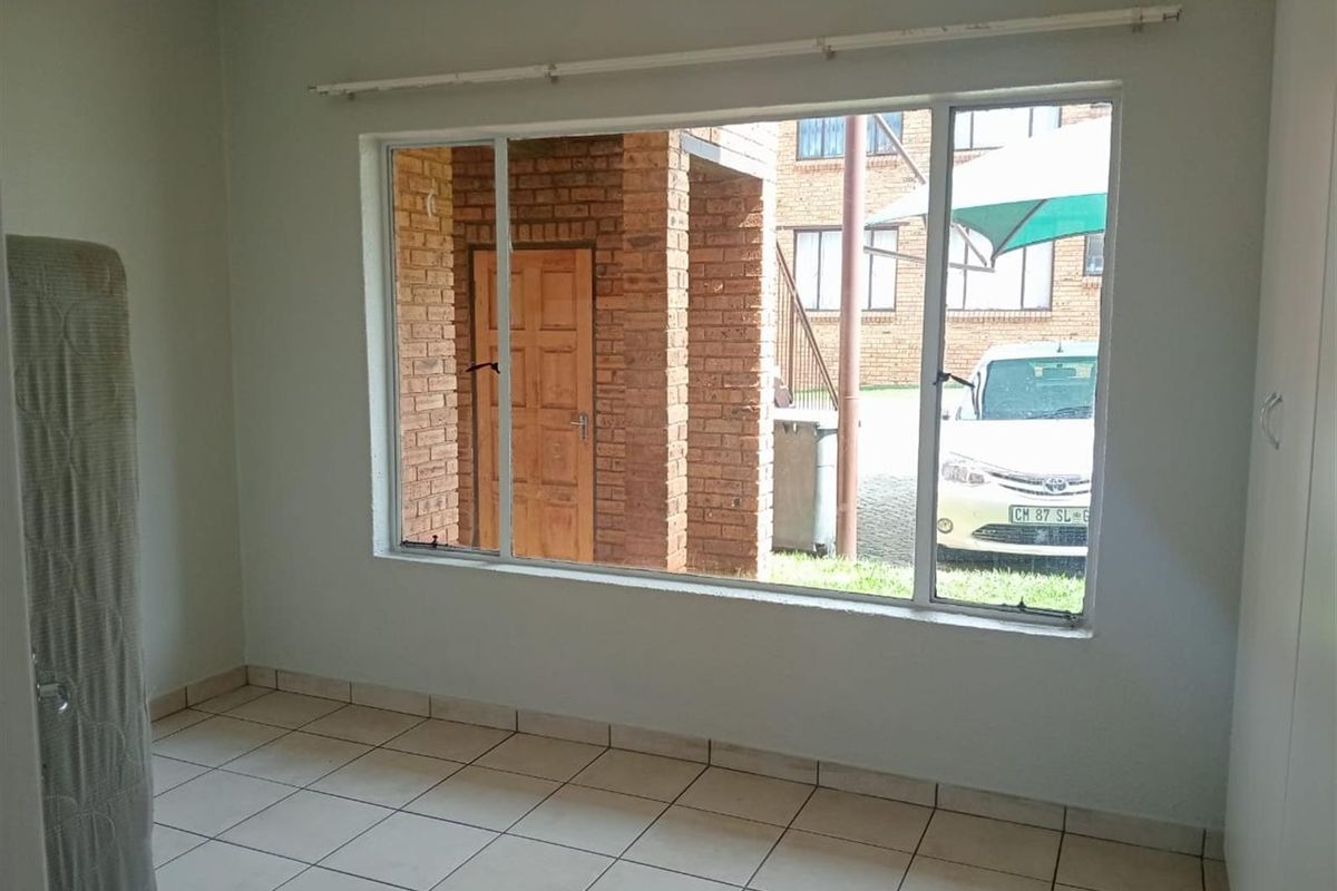 A bright, empty bedroom featuring tiled flooring and a large window overlooking the exterior complex area.