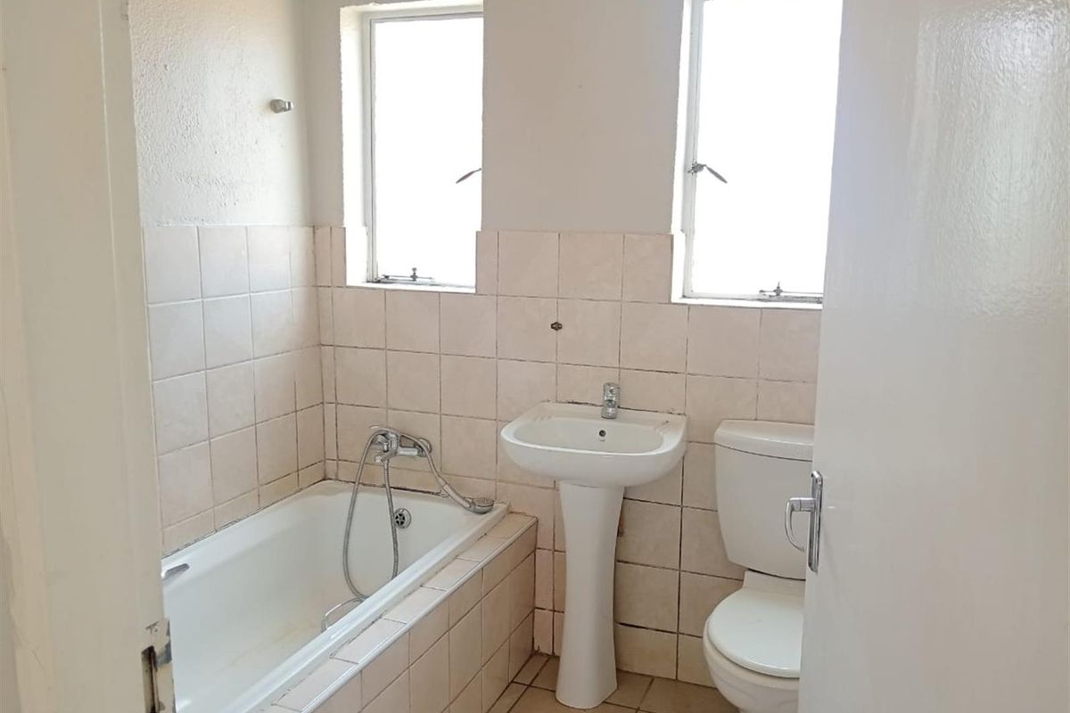 A dated bathroom featuring a standard bathtub with handheld shower attachment, pedestal basin, and toilet, finished with neutral wall tiles.