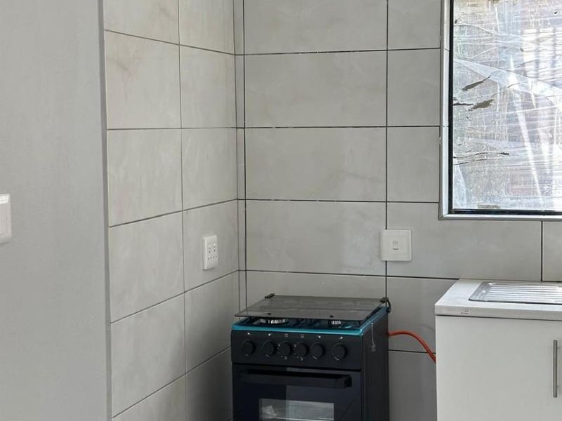 A compact kitchen area featuring tiled walls, a freestanding stove, and basic cabinetry with a sink.