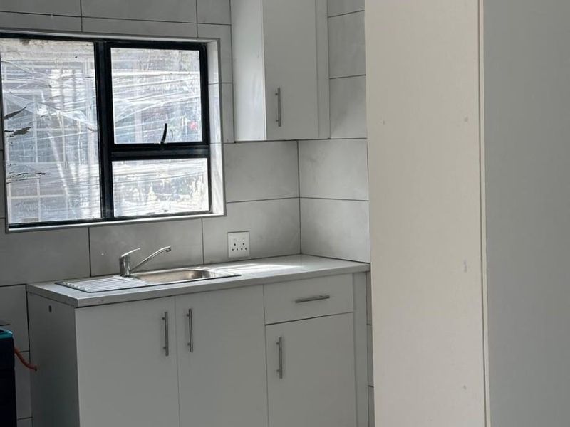 A clean, modern kitchen featuring white built-in cabinetry, a stainless steel sink, and neutral wall tiling, offering a bright and functional workspace.