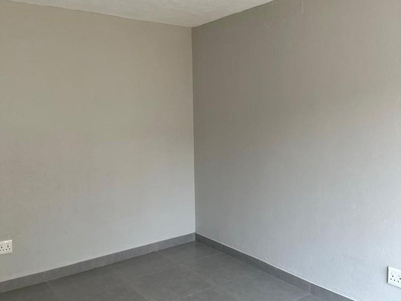 A clean, empty bedroom featuring neutral grey wall paint and modern grey floor tiles with integrated electrical outlets.