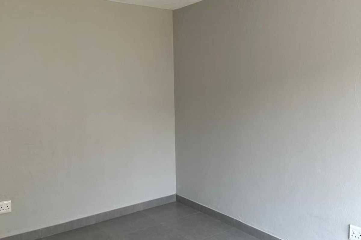 A clean, empty bedroom featuring neutral grey wall paint and modern grey floor tiles with integrated electrical outlets.