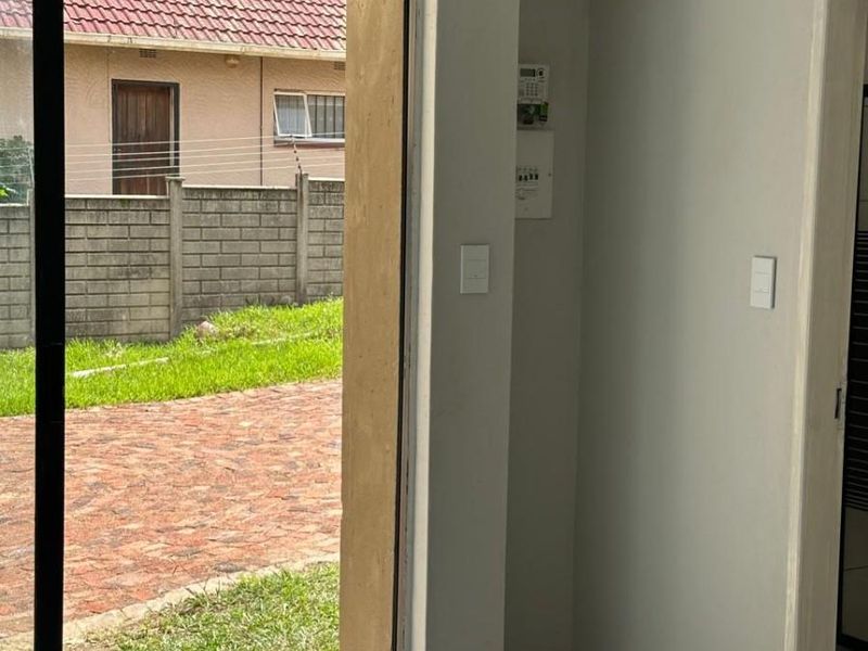 A bright, empty living area featuring modern tiled flooring and a large sliding glass door providing direct access to the outdoor garden space.