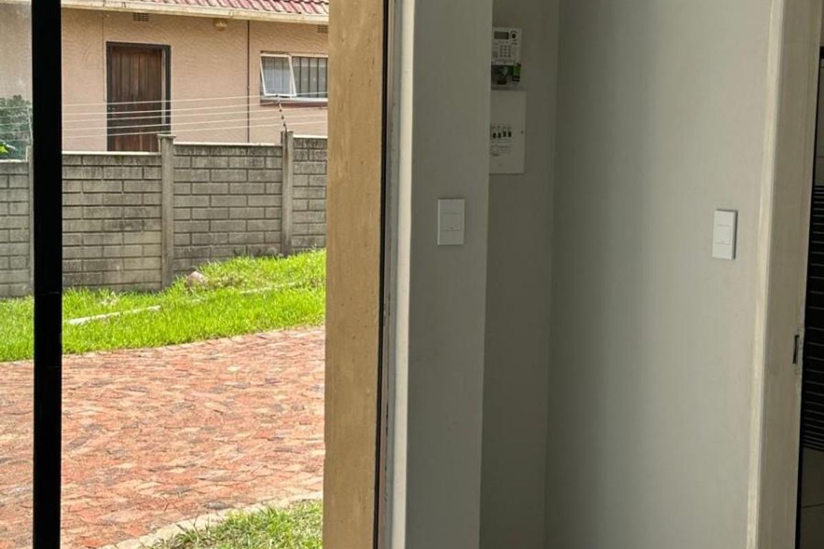 A bright, empty living area featuring modern tiled flooring and a large sliding glass door providing direct access to the outdoor garden space.