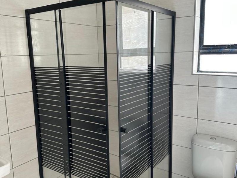 A modern bathroom featuring a black-framed glass shower enclosure with a rain shower head, tiled walls, and a standard toilet.