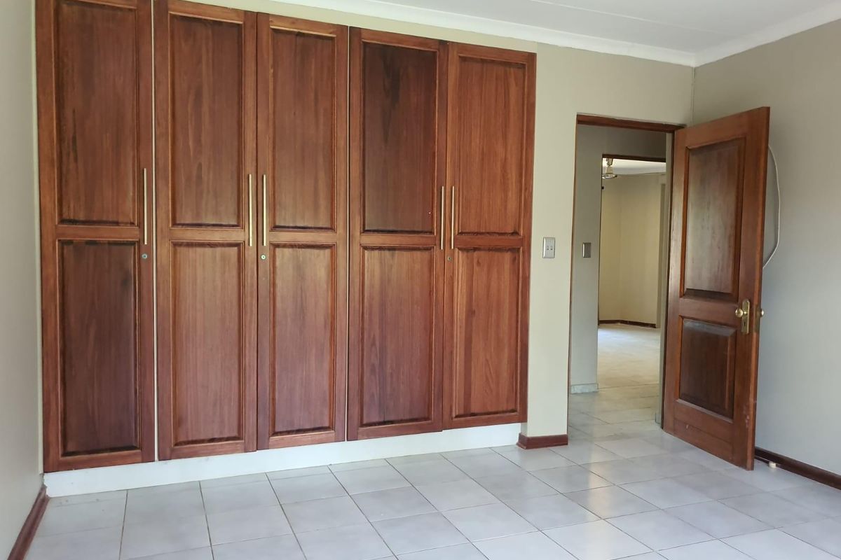 A spacious bedroom featuring built-in wooden cupboards, tiled flooring, and a ceiling fan, offering a clean and functional living space.
